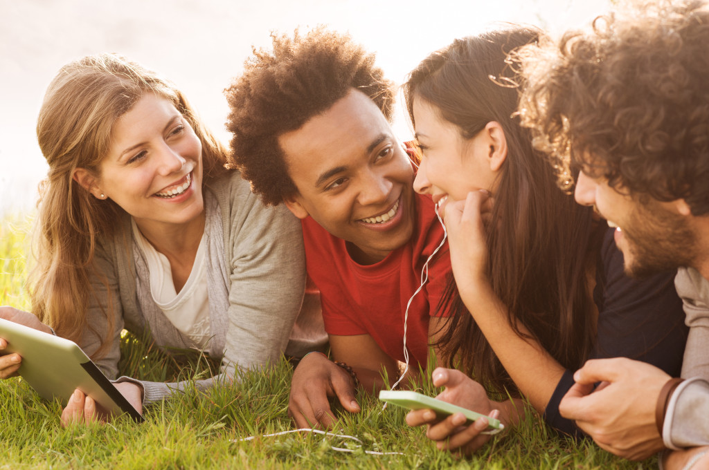 Group Of Young Multiracial People Holding Digital Tablet And Cellphone Outdoor